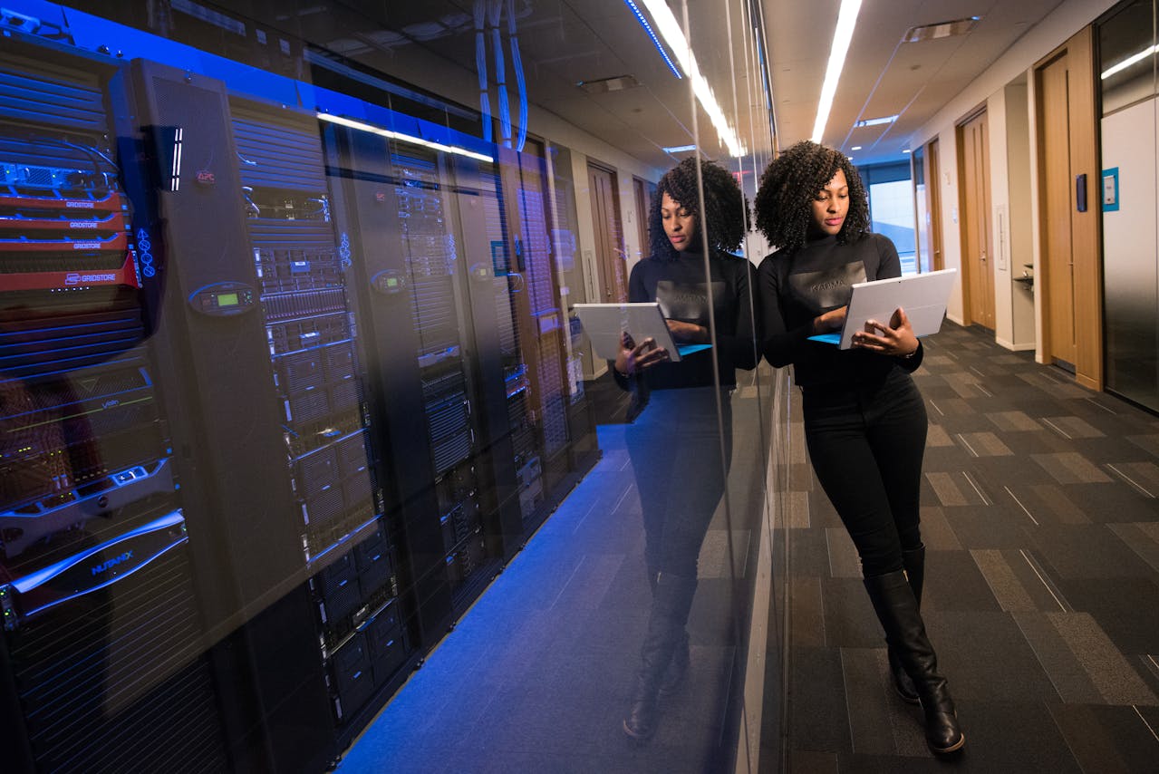 Picture of a woman leaning up against a server cabinet, holding a laptop – WinuSoft | Web Hosting and Maintenance for WordPress Websites